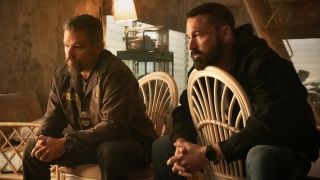 From left to right: Matt Damon and Ben Affleck sitting in chairs with their hands clasped together.
