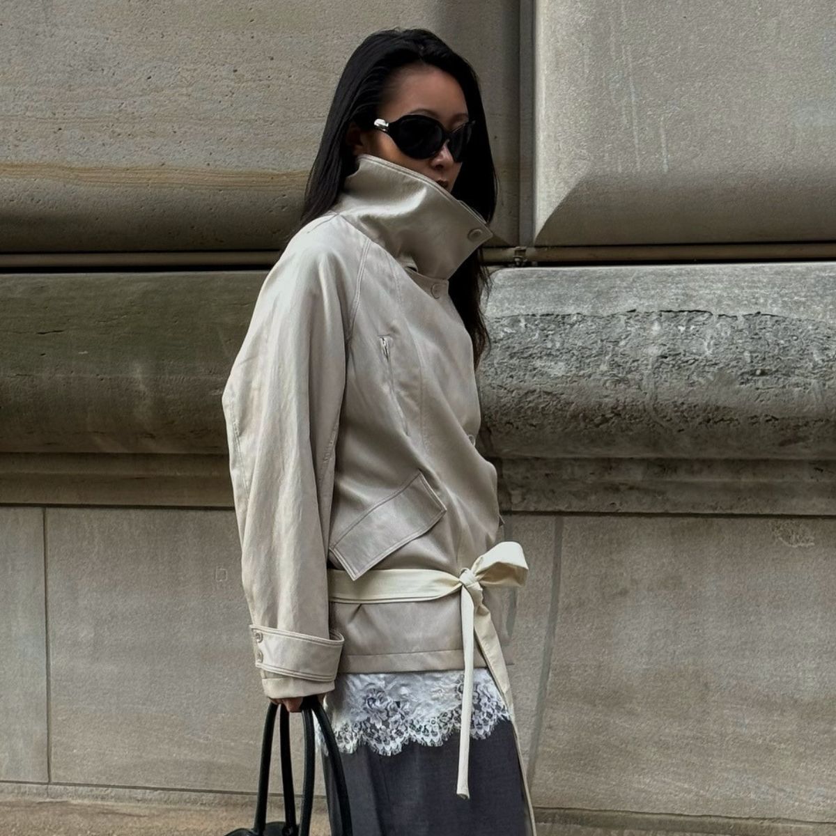Caroline wears a funnel-neck trench coat, lace top and tailored trousers
