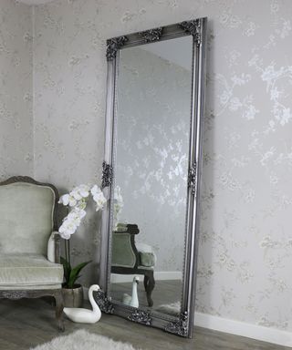A room with silver metallic walls, a rectangular silver standing full-length mirror, and a gray armchair to the left of it
