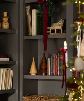 dark gray bookshelves decorated for christmas with mini christmas trees, a sleigh, snowman and a small wreath