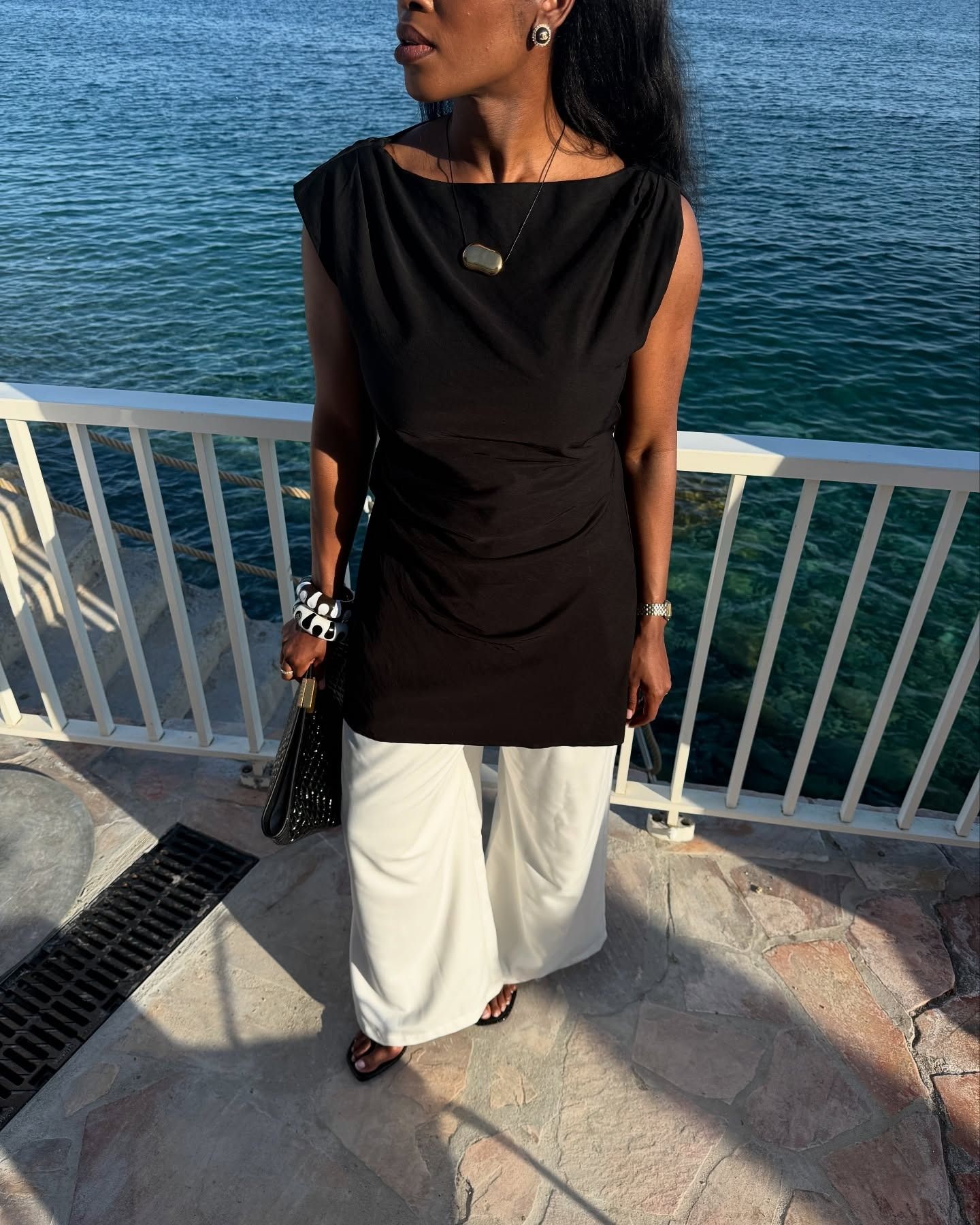Influencer Marilyn wearing a black boatneck tunic, white trousers, and black-and-white bangles.