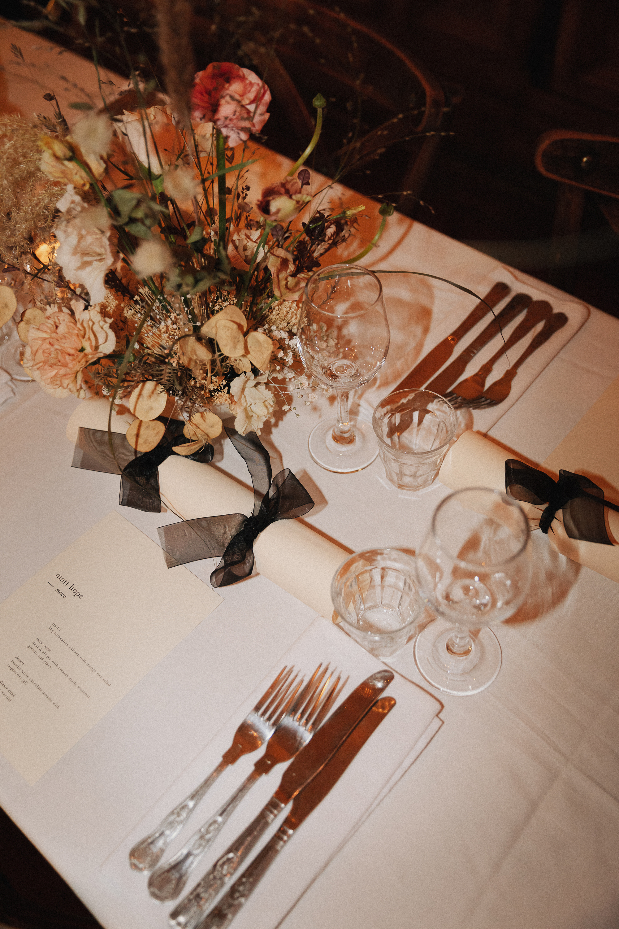 table setting with floral centerpiece, with silverware, paper crackers, written menu and glassware