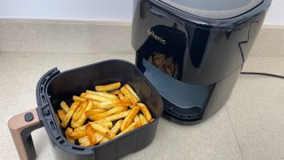 En svart airfryer av typen Ultenic K10 står på en köksbänk med behållaren fylld med frysta pommes frites, redo att tillagas.