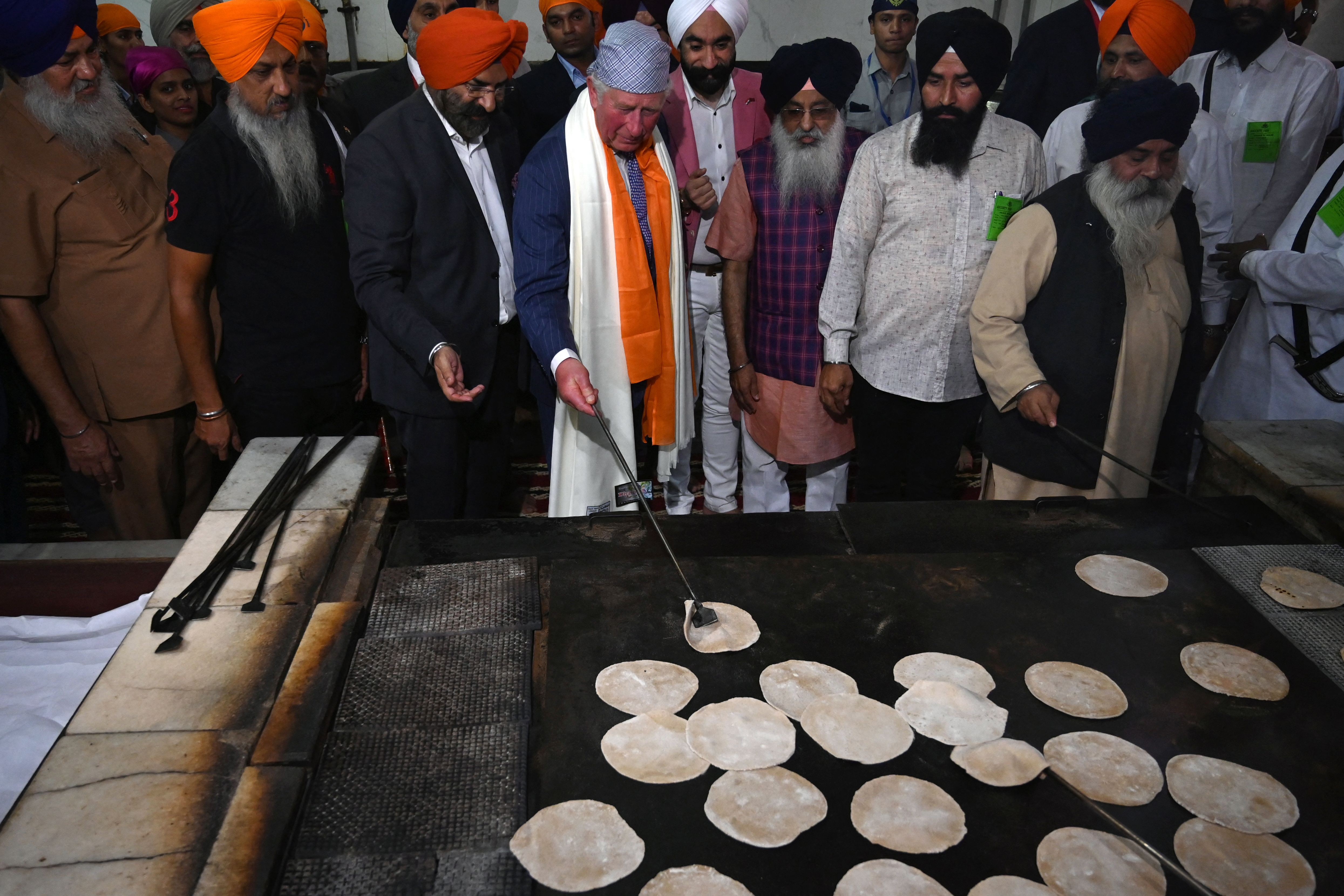 King Charles making chapati bread in India surrounded by a group of men