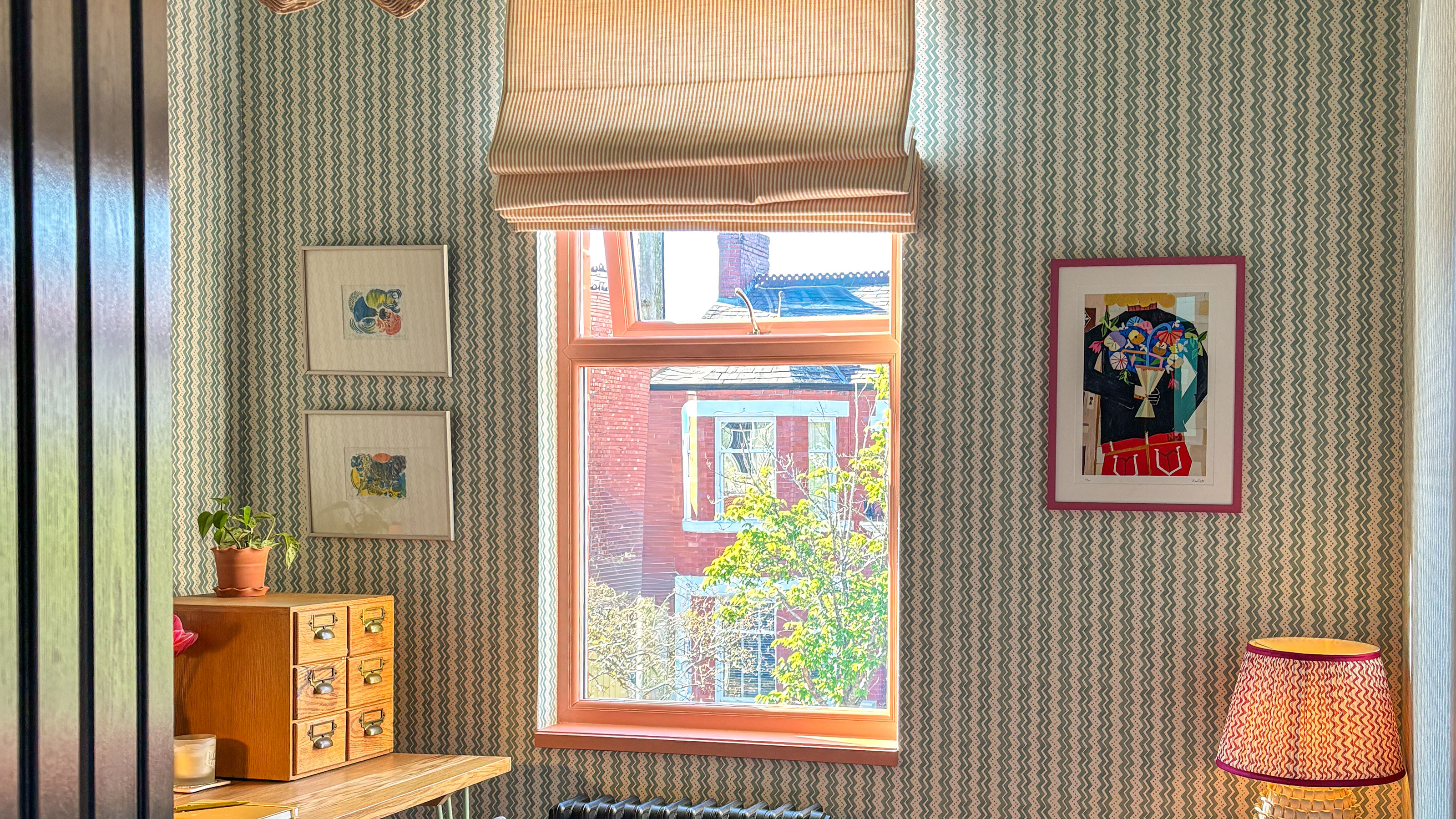 Home office with striped wallpaper, black radiator, wooden desk and striped blind on window