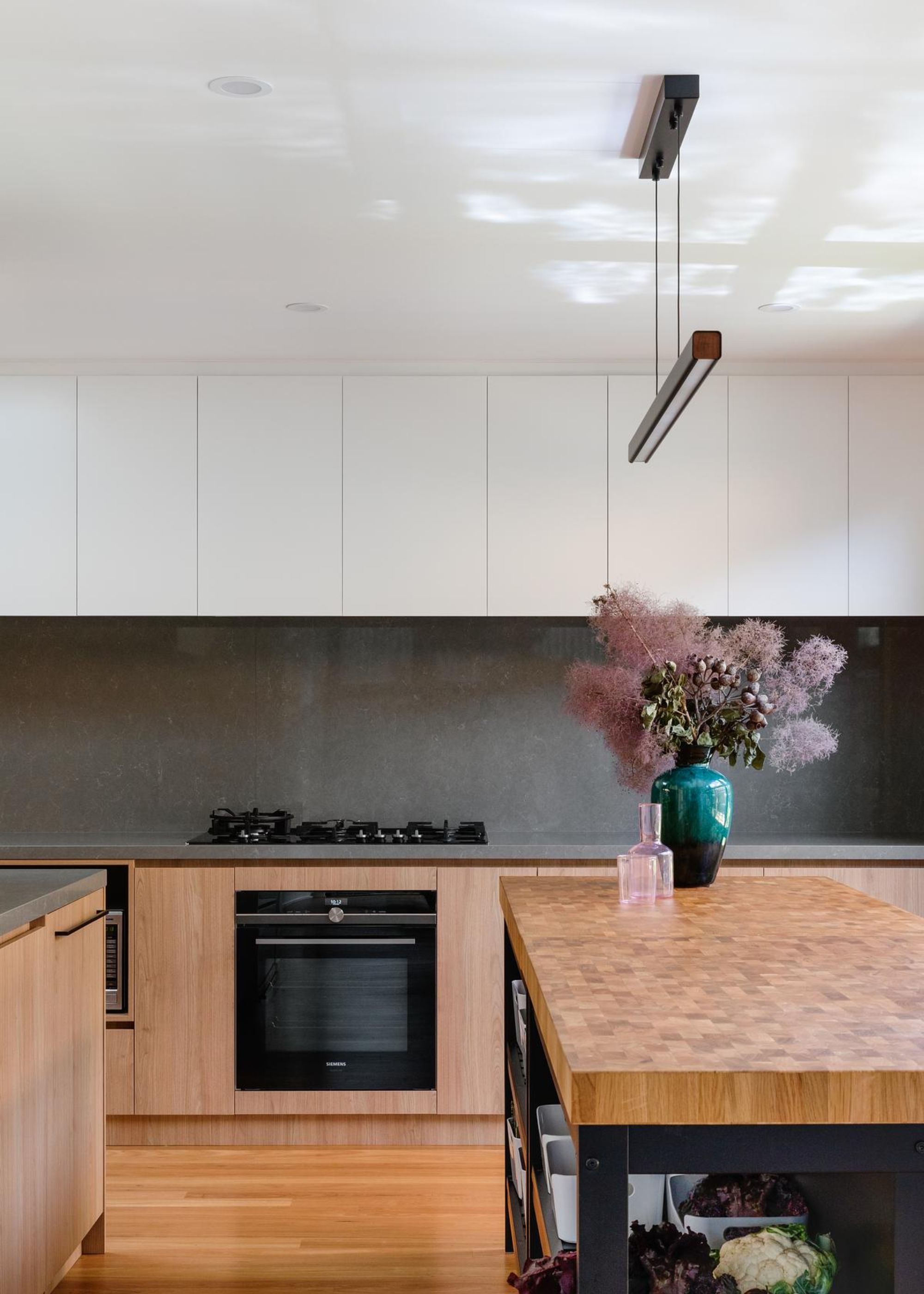 A kitchen with a conventional oven as well as a gas stove top. There is also a large kitchen island with a vase and flowers inside of it