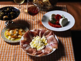 food view, olives, capreses salad, cured ham and cheese and beans with wine glasses on orange table cloth