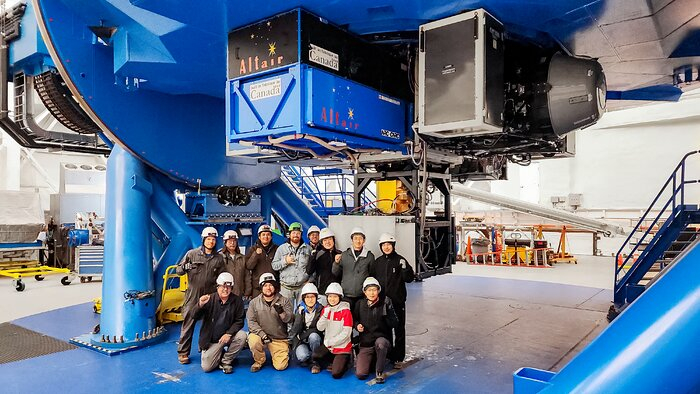 Un grupo de personas con cascos de seguridad de pie debajo de parte de una gran máquina industrial azul.