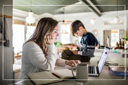 Mum working on laptop while her son sits on the desk nearby