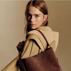 Young woman wearing S&eacute;zane trench coat and brown suede bag.