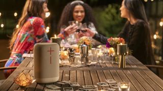 Ultimate Ears Epicboom speaker on a table, with women sharing drinks in the background