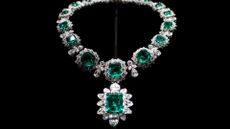 A necklace with large emeralds and diamonds against a black background