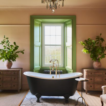 A bedroom colour drenched in Farrow & Ball's Setting Plaster pink paint with a bathtub in the middle of the room and the bay window painted in Farrow & Ball Yeabridge Green