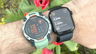 Close-up of the Garmin Instinct 3 in teal on a user's wrist next to an all-black Apple Watch Series 10m on a dark blue band