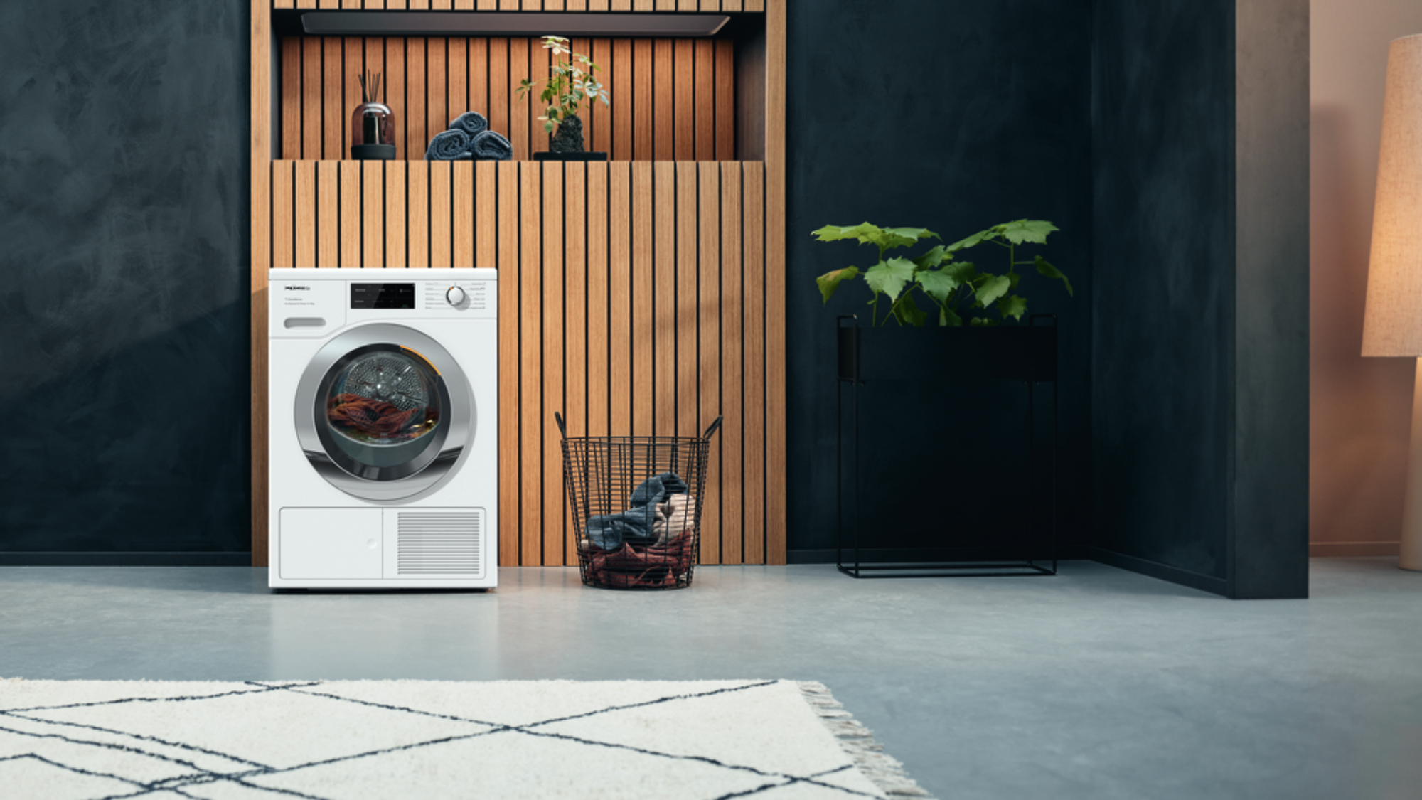 heat pump tumble dryer in modern utility space with grey floor, dark grey wall and wooden slatted cabinet