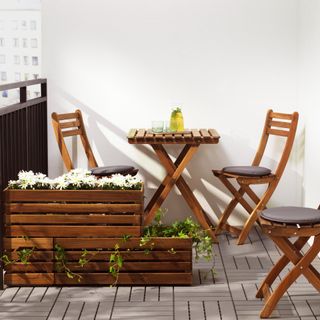 Wooden window box planters with white flowers and ivy on small balcony with matching wooden garden bistro set