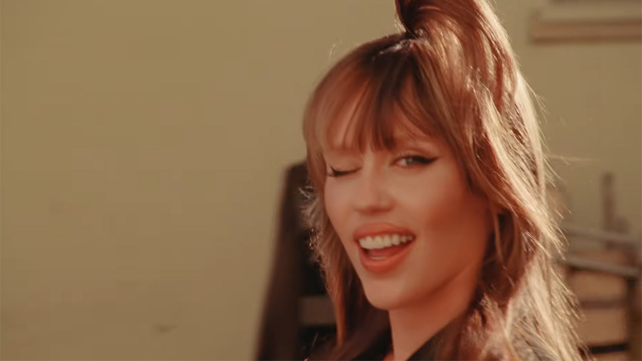 Miley Cyrus winking at the camera while walking in her 2025 Something Beautiful film.
