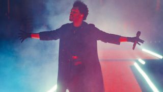 The Weeknd standing on stage in front of a pink light in The Weeknd: Live at SoFi 