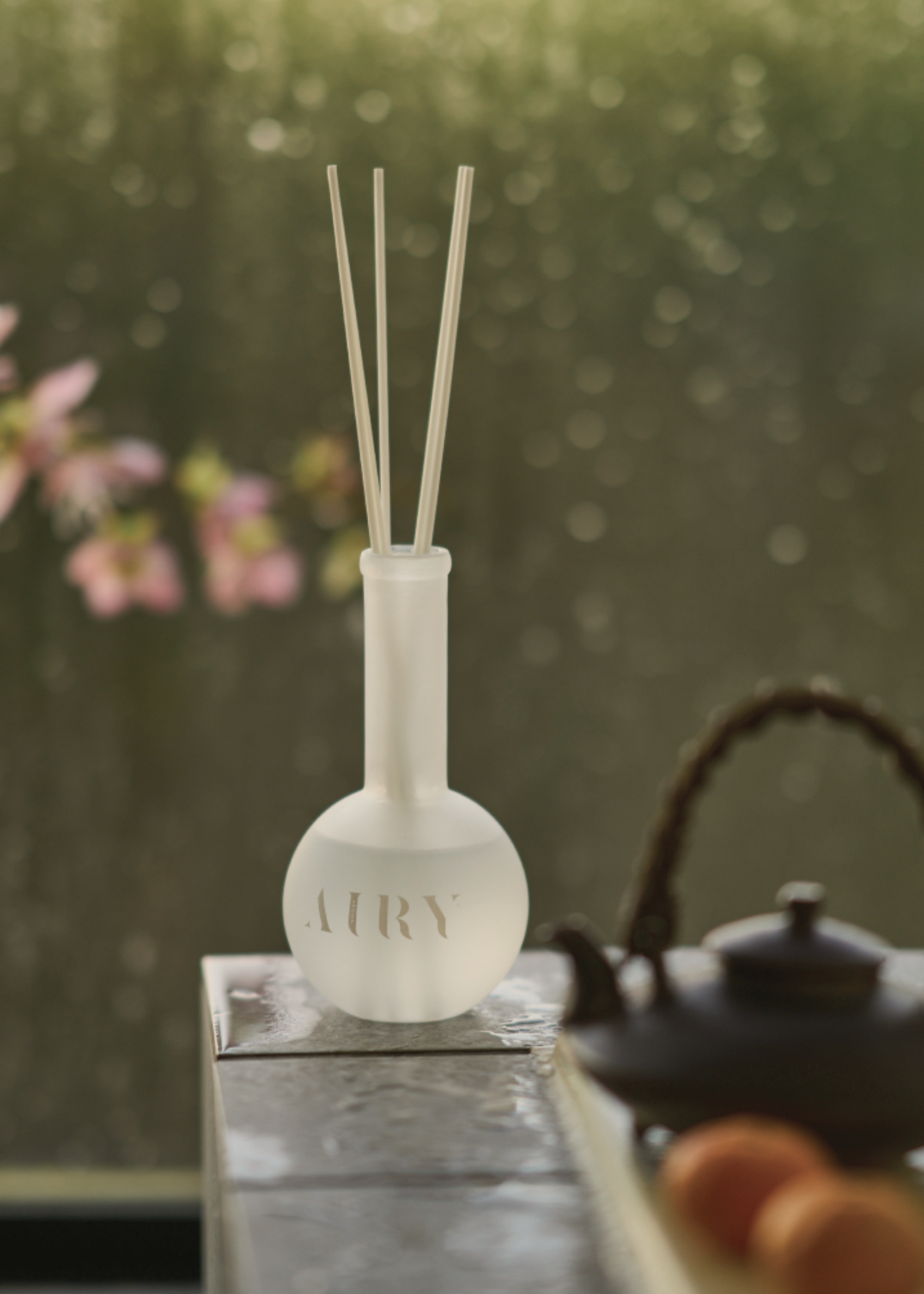 A glass vase reed diffuser on a table by a teapot