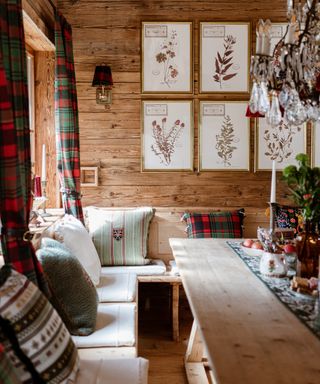 winter decor ideas, cozy cabin style dining room with wood clad walls, wood bench seating, chandelier, tartan drapes and cushions, botanical prints on the wall