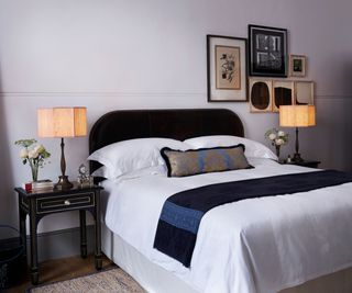 A bed at NoMad London next to two bedside tables decorated with antique lamps and flowers