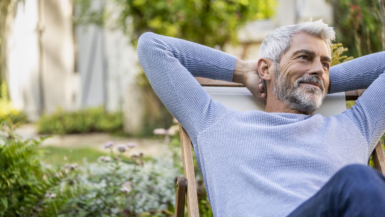 An older man relaxes in a chair outside.