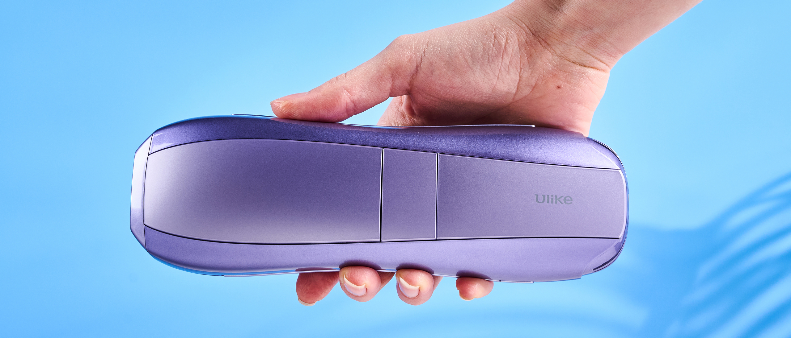 hand holding the ULike Air 10 IPL machine photographed in front of a blue background. 