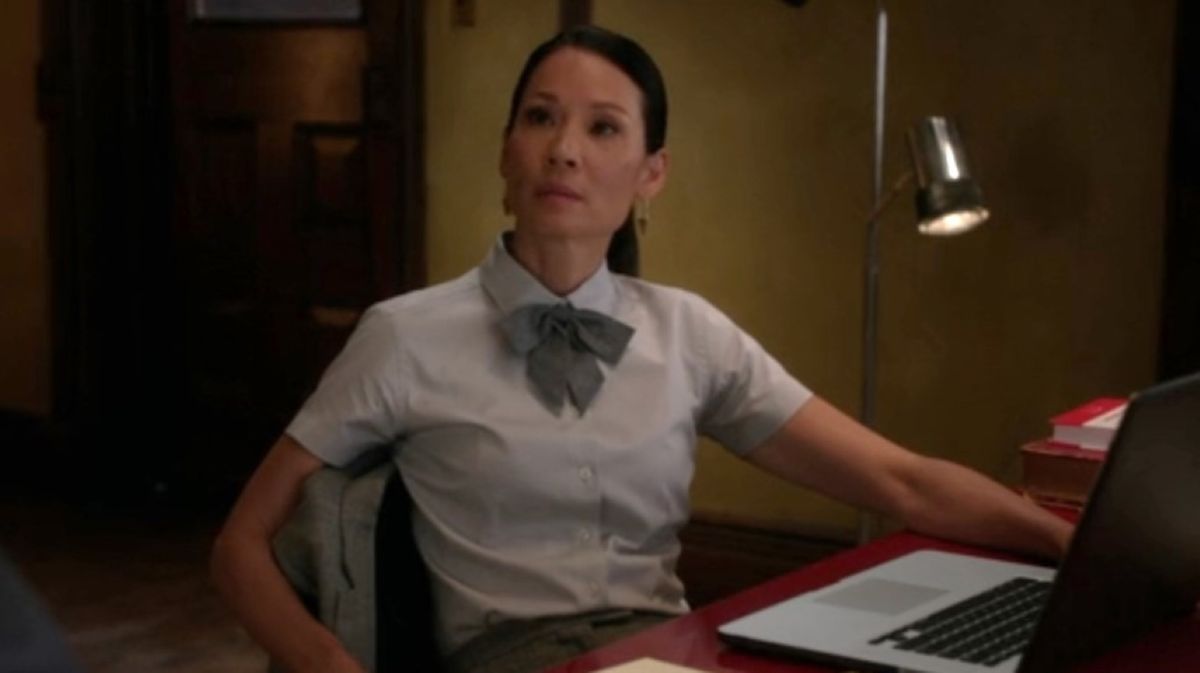 Lucy Liu as Watson sitting at a table listening to Sherlock in Elementary