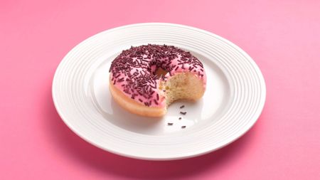 Pink doughnut on white plate on pink background with bite removed