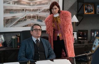 matthew broderick as a guest star sitting at his desk and carrie preston as elsbeth looking over him in a big pink coat on elsbeth season 2