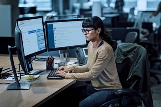 Brunette woman sitting on a desk with multiple computer monitors