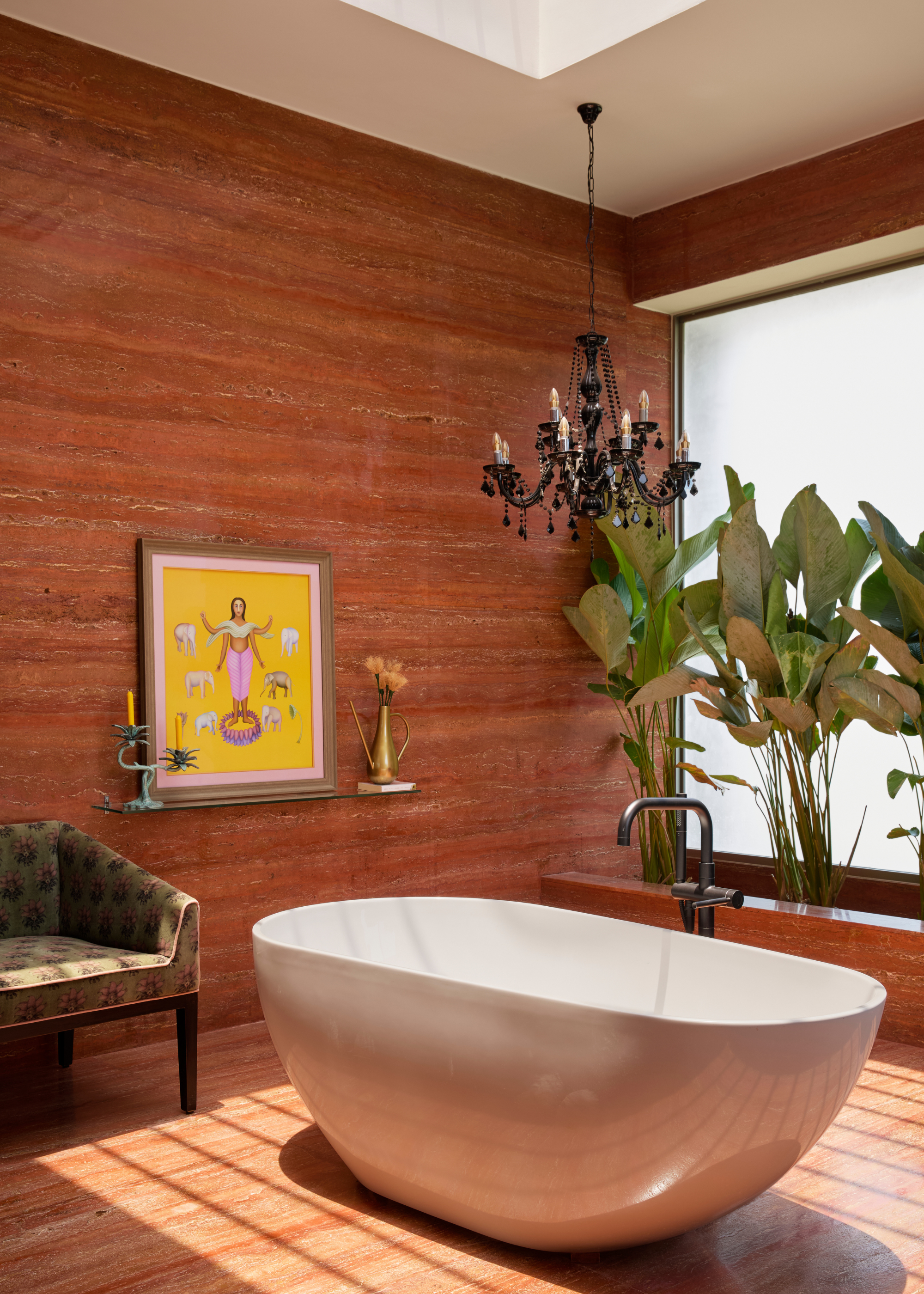 A bathroom with orange stone walls, a floating vase with a vase and a candlestick, a sofa seat, a hanging black chandelier, and a bath tub