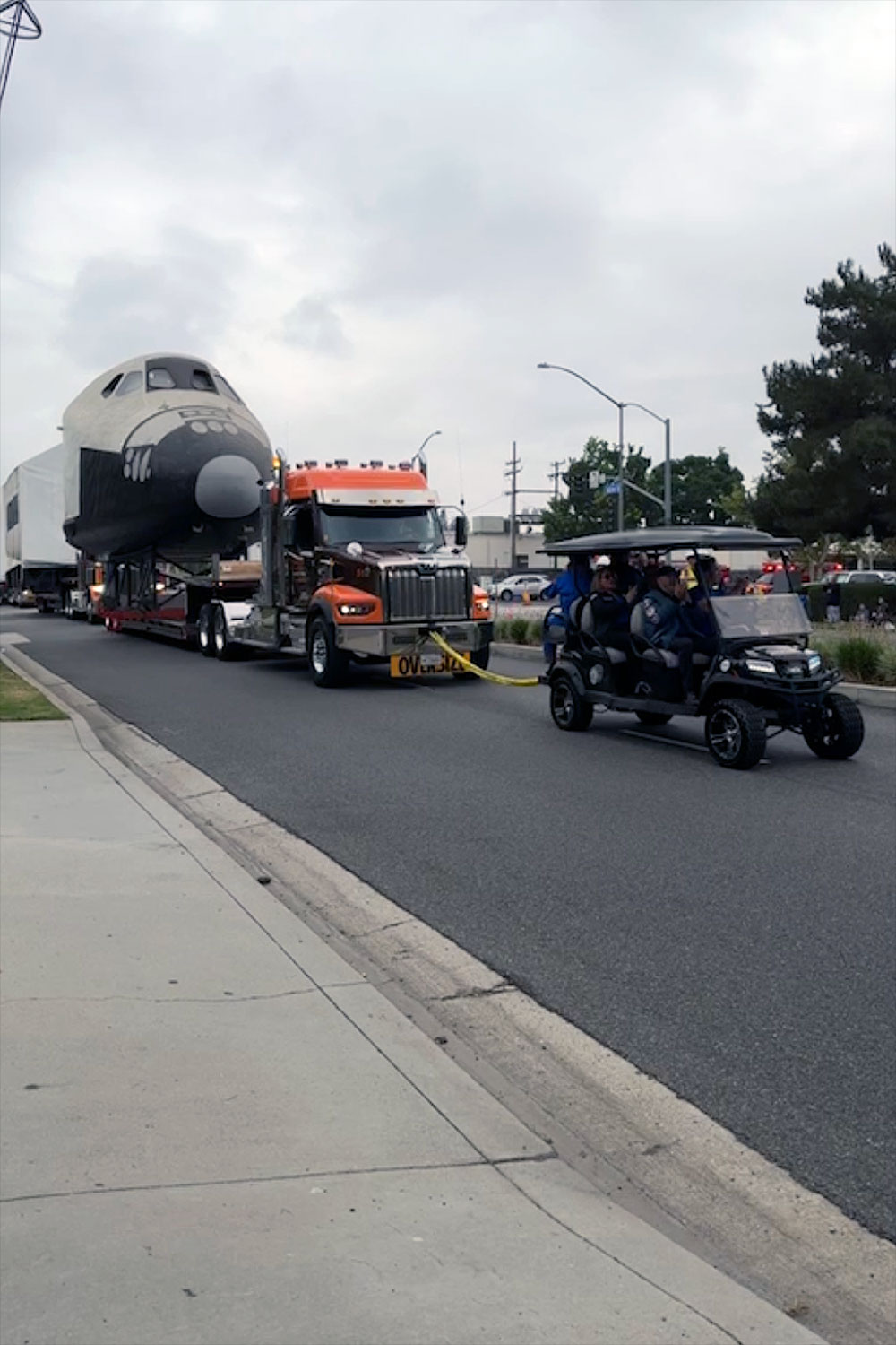 A semi-trailer truck tows a full-size space shuttle mockup down a city street