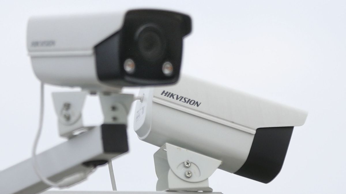 A slightly out of focus CCTV camera points at a 45 degree to the right of the viewer, while a second camera that is in focus bearing the word &amp;#039;Hikvision&amp;#039; points away from the viewer