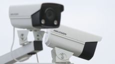 A slightly out of focus CCTV camera points at a 45 degree to the right of the viewer, while a second camera that is in focus bearing the word 'Hikvision' points away from the viewer