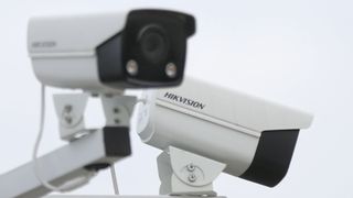 A slightly out of focus CCTV camera points at a 45 degree to the right of the viewer, while a second camera that is in focus bearing the word 'Hikvision' points away from the viewer