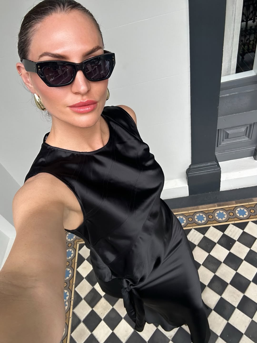 aymie cahill wears a black satin slip dress and black sunglasses