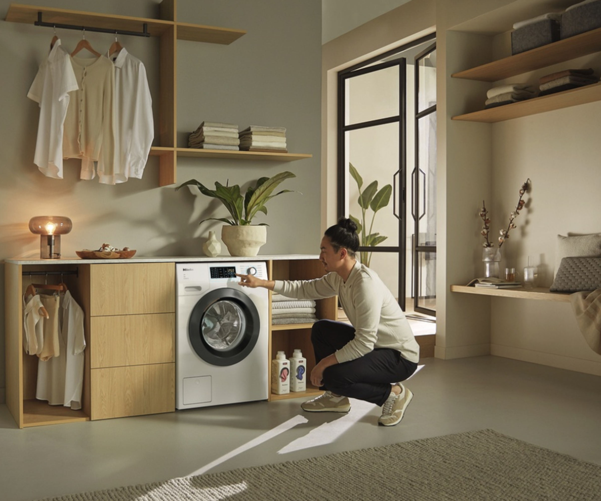 open plan utility area with grey floor and man crouching in front of washing machine