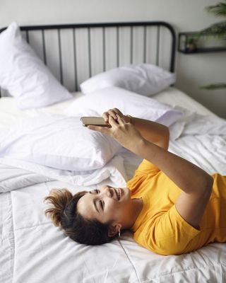 A woman looks at her phone while laying on a bed