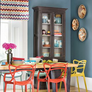 Blue dining room with patterned blinds, colourful chairs and wall decor