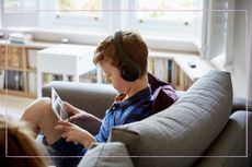 A young boy sat on a sofa using a tablet while wearing headphones