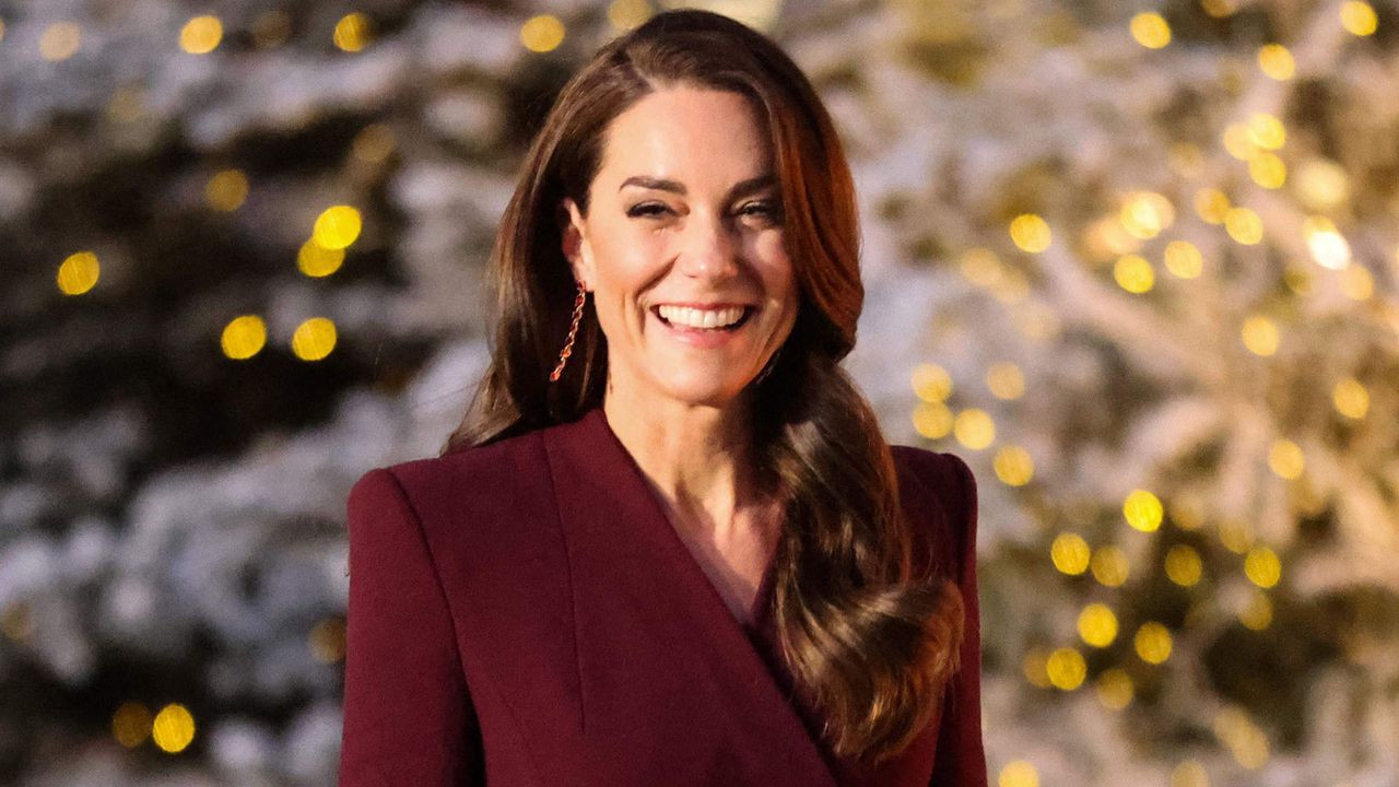 Kate Middleton in a burgundy coat in front of trees decorated for Christmas