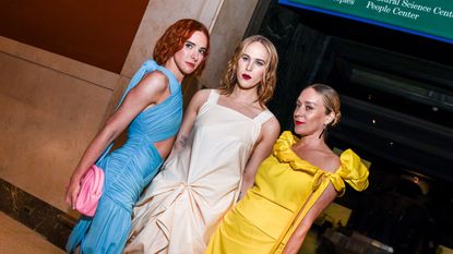 Three women with different colored hair and gowns pose.