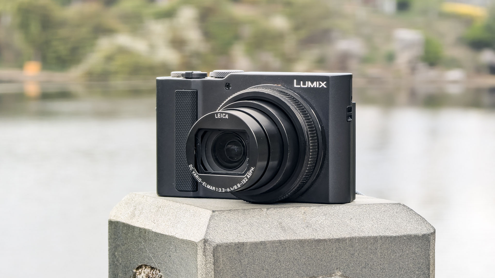 Panasonic Lumix TZ300 compact camera placed on a bridge with a scenic mountain backdrop