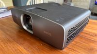 The BenQ W2720i projector, pictured on a wooden table in a living room