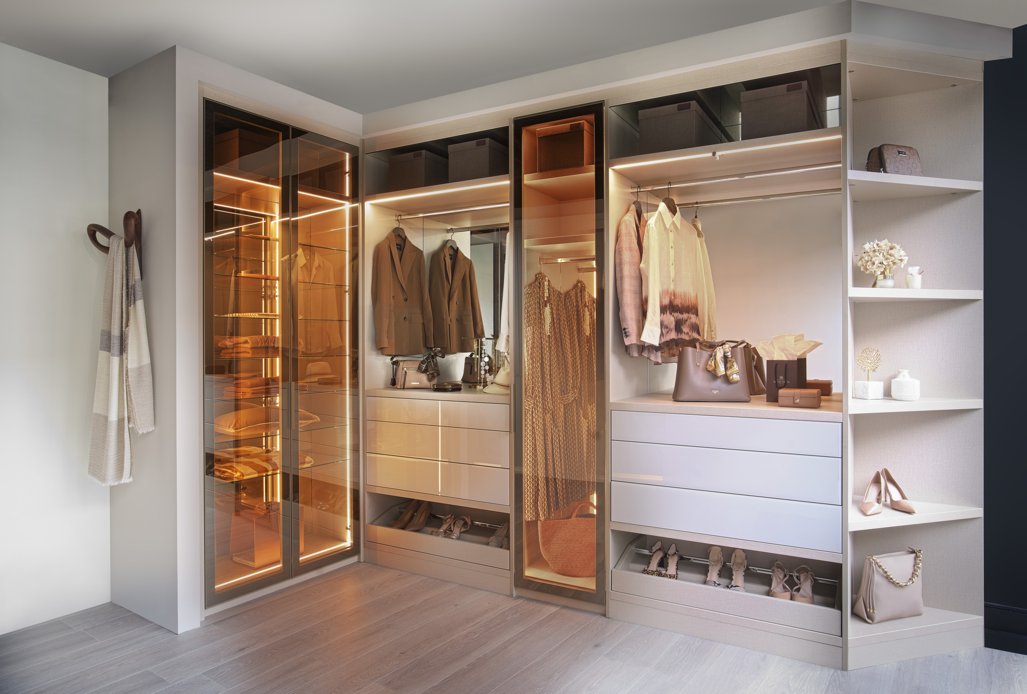 A built-in closet with glass doors, corner shelves, and organized clothes on rails