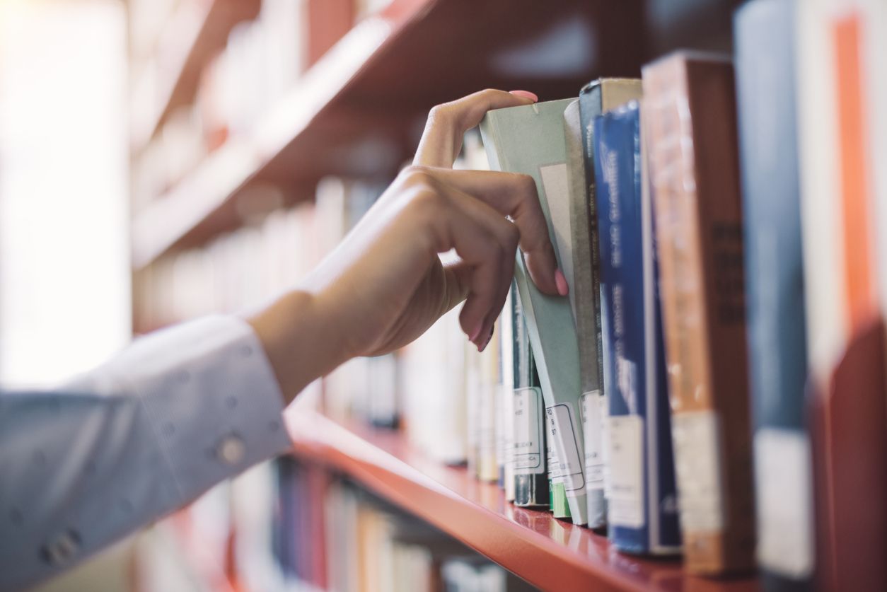 A woman grabs a library book from the shelf.