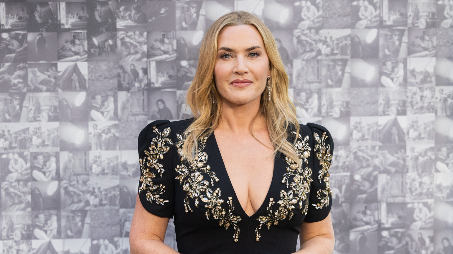 Kate Winslet wearing a loose wave hairstyle. She is wearing a black dress with ornate detailing around the plunging neckline. 