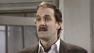 Basil Fawlty exasperated next to a corpse in a basket in Fawlty Towers