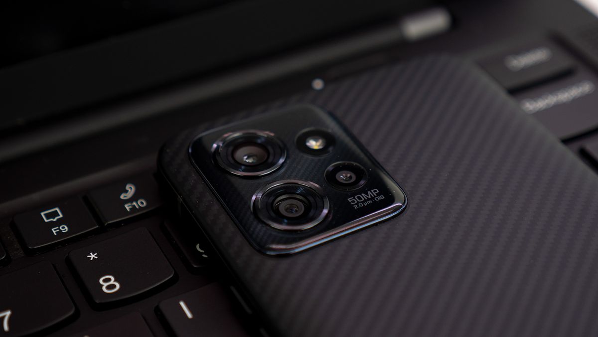 The camera island of the ThinkPhone by Motorola on a Lenovo ThinkPad Carbon X1 laptop